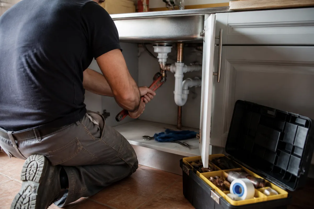 Self-employed plumber from behind repairing a pipe under a sink, no face visible